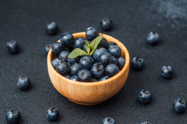 Taze yaban mersiniyle dolu bir kase ve karanlık bir yüzeye yerleştirilmiş bir nane filizi..