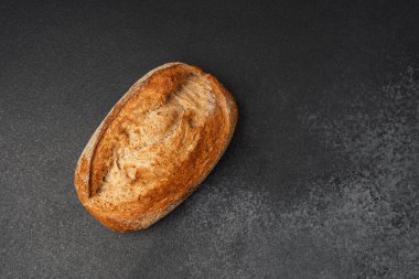 Bir somun taze pişmiş zanaatkar ekmeği koyu bir tezgahın üzerinde duruyor..