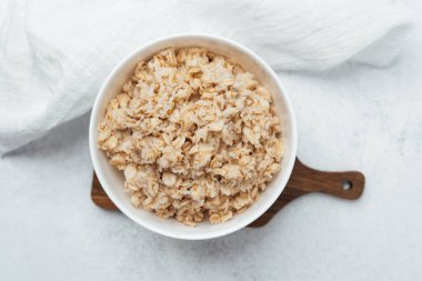 Bir kase sıcak yulaf ezmesi, yumuşak bir bezle çevrili ahşap bir tahtanın üzerinde oturur..