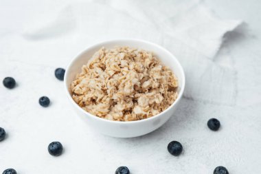 Hafif bir yüzey üzerinde taze yaban mersinleriyle çevrili bir kase sıcak yulaf ezmesi..