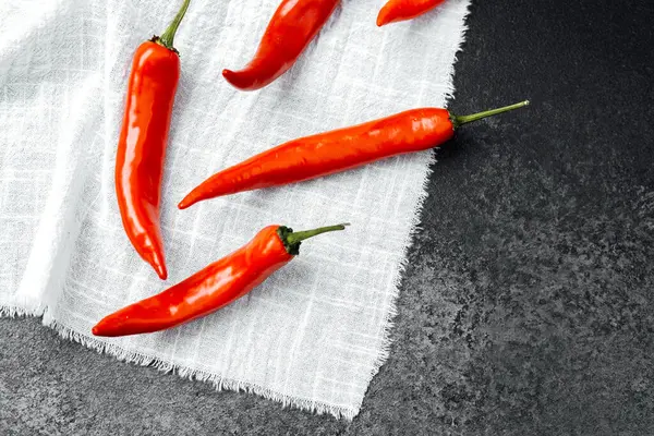 Koyu bir yüzeye karşı beyaz keten kumaş üzerine dizilmiş parlak kırmızı biber..