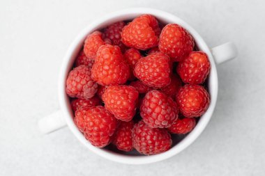 Organik gıda veya vegan diyet konsepti için hafif yüzeyde beyaz kasede ahududu.