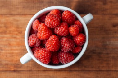 Beyaz kasede ahududu. Kırsal gıda tasarımı ya da organik yeme konsepti için ahşap masa üzerinde
