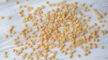 Küçük sarı kuru bezelyeler, besin değeri yüksek ve çok yönlü besin maddelerini ön plana çıkaran parlak beyaz ahşap bir yüzeye rastgele dağılır..