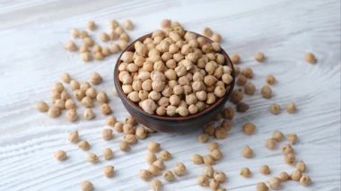 Kuru çiğ bezelyeler, hafif desenli ahşap bir yüzeye yerleştirilmiş, kabın etrafına saçılmış kırsal kahverengi bir kâseyi doldurur..