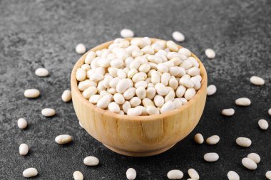 Beyaz fasulyeler, vejetaryen protein, sağlıklı yiyecek veya mutfak düzeni konsepti için siyah taş zemine saçılmış.