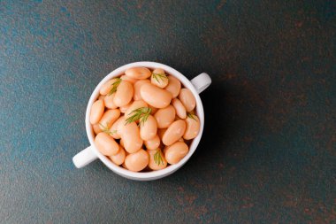 Sağlıklı yemek, vejetaryen diyeti veya gıda tasarım konsepti için siyah kumaş üzerine otlar seramik kasede beyaz tereyağlı fasulye.