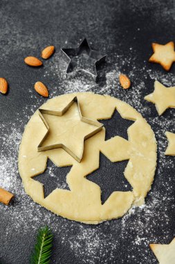Yemek blogu ve mevsimlik tarif konsepti için karanlık masa üzerinde un ve malzemelerle pişirilmiş Noel yıldızı kurabiyeleri.
