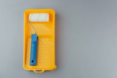 Ev geliştirme ve yenileme konsepti için gri arka planda sarı tepsinin içinde mavi saplı boya silindiri