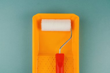 Yeşil arka planda sarı tepside kırmızı saplı boya silindiri DIY yenileme ve ev geliştirme konsepti için