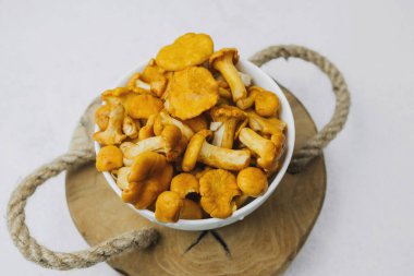 Bir kase dolusu canlı chanterelle mantarı ahşap bir tahtanın üzerinde duruyor..