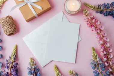 Kurdeleli hediye kutusu, zarf, çiçekler ve pembe arka planda mum.