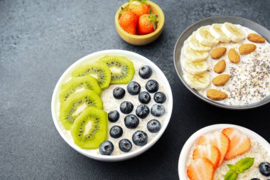 Çeşit çeşit kahvaltı yulaf ezmesi kaseleri, içinde meyve çili tohumları ve siyah arka planda bademler var.