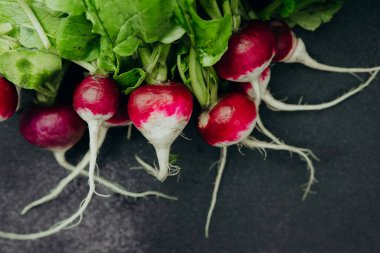 Koyu arkaplanda yeşil yapraklı taze kırmızı turplar.