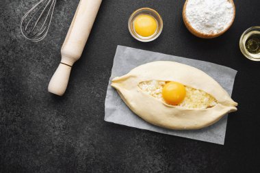 Parşömen üzerinde peynir ve sarısı olan Khachapuri ve koyu mutfak masası.