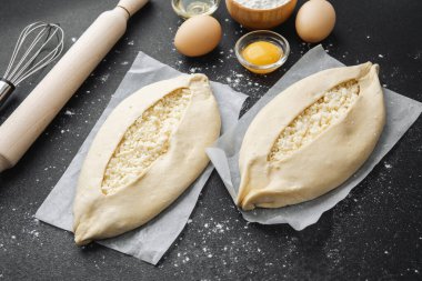 Malzemelerin üst görüntüsü ve iki pişmemiş khachapuri un kaplı siyah masa üzerinde