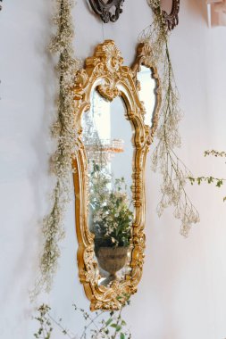 Eski bir altın ayna, çiçekli süslemelerle dolu huzurlu bir iç mekanı yansıtır..