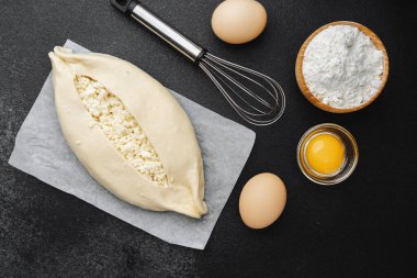 Süzme peynirli çiğ khachapuri ve siyah arka plandaki malzemeler.