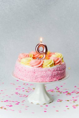 Pembe ve sarı şekerli bir pasta ve kutlama için bir mum..