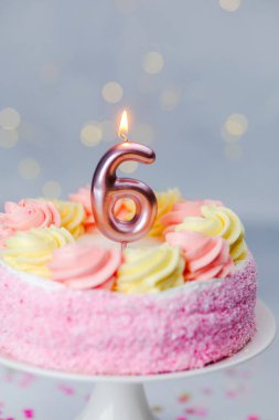 Renkli güllerle süslenmiş pembe kremalı pasta ve parlayan altı mum..