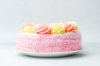 Süslü kremayla süslenmiş göz kamaştırıcı pembe ve sarı bir pasta beyaz bir tabakta duruyor..