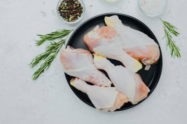 Biberiye ve baharatlı siyah tabakta çiğ tavuk budu.