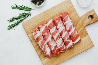 Domuz pastırmasına sarılı sosisli börekler, ahşap tahtada otlarla.