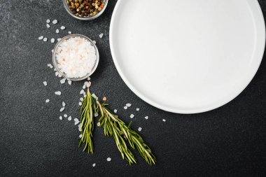 Siyah taş zemin üzerinde bitkiler ve baharatlar olan boş beyaz tabak