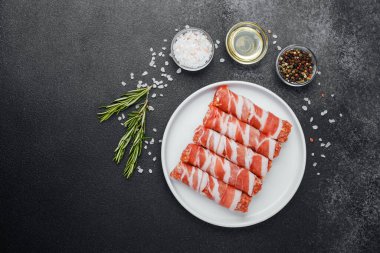 Çiğ domuz pastırması beyaz tabağa sarılmış, baharatlı ve otlu.