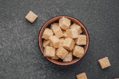 Kahverengi şeker küpleriyle dolu bir kase koyu bir tezgahın üzerinde duruyor..