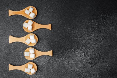 Siyah yüzey üzerinde yaratıcı bir düzende sergilenen şeker küplü tahta kaşıklar.