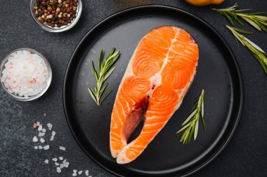Siyah tabakta taze otlar ve baharatlarla süslenmiş taze somon filetosu..