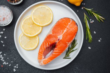 Limon dilimleri ve pişirmeye hazır bitki dallarıyla sergilenmiş taze somon filetosu..