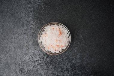 Siyah taş zemin üzerinde pembe himalaya tuzu dolu cam kase.