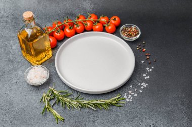 Boş beyaz tabak, zeytinyağı biberiye biber, tuz ve kiraz domatesli koyu masa.