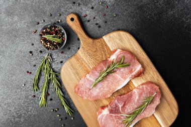 Biberiyeyle süslenmiş iki çiğ domuz pirzolası ve yanında baharatlar..