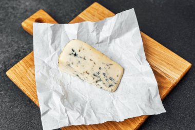 Buruşmuş kağıda sarılı bir parça mavi peynir tahta üzerinde duruyor..