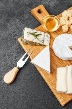 Bal ve peynir bıçağıyla ahşap bir tahtaya dizilmiş peynir çeşitleri..