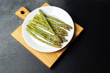 Yeşil kuşkonmaz mızrakları hafifçe tatlandırılmış ve beyaz bir tabakta ahşap üzerine dizilmiş..