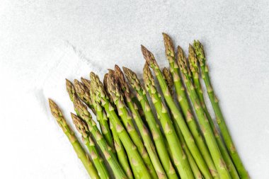 Bir grup taze yeşil kuşkonmaz mızrağı hafif bir arka planda dinleniyor..