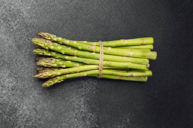Canlı yeşil kuşkonmaz sicimle bağlanmış koyu dokulu bir yüzeye dayanır..