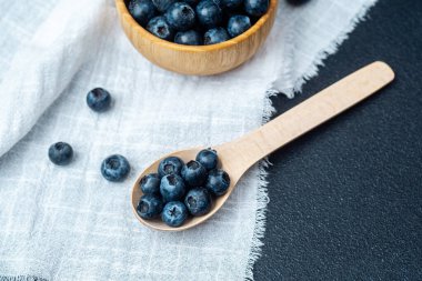 Taze toplanmış yaban mersini ahşap bir kasede dinleniyor ve kaşık keten kumaşın üzerinde..