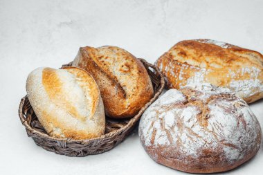 Zanaatkar ekmek çeşitleri tarafsız tonlarla dokunmuş bir sepetin içinde zarif bir şekilde dizilmiştir..