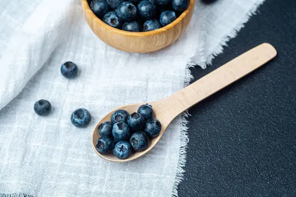 Taze toplanmış yaban mersini ahşap bir kasede dinleniyor ve kaşık keten kumaşın üzerinde..