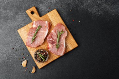 Tahtaya yerleştirilmiş çiğ domuz pirzolası, biberiye ve baharatla süslenmiş..