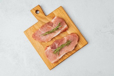 Odun kesme tahtasına konmuş iki pişmemiş domuz pirzolası..