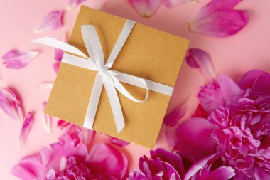 Beyaz kurdeleli hediye kutusu ve pastel arka planda pembe şakayıklar.