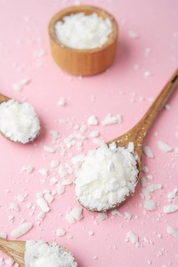 Pastel pembe arka planda soya mumu tanecikli çoklu tahta kaşıklar.