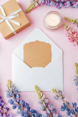 Pembe arka planda kart ve çiçeklerle birlikte hediye kutusu ve zarf