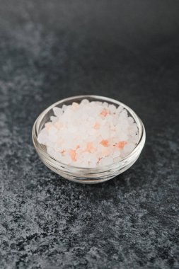 Siyah taş zemin üzerinde pembe himalaya tuzu dolu cam kase.